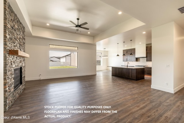 unfurnished living room featuring dark wood-type flooring, a fireplace, a raised ceiling, and ceiling fan