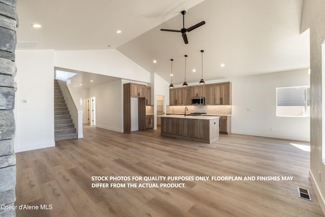 kitchen with sink, decorative light fixtures, light hardwood / wood-style flooring, ceiling fan, and a kitchen island with sink