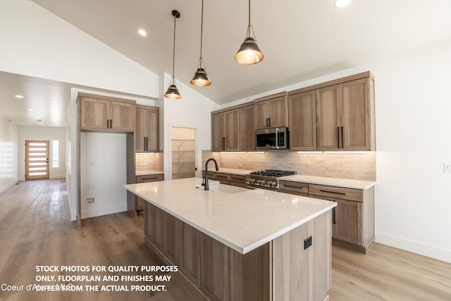 kitchen with pendant lighting, sink, backsplash, stainless steel appliances, and a center island with sink