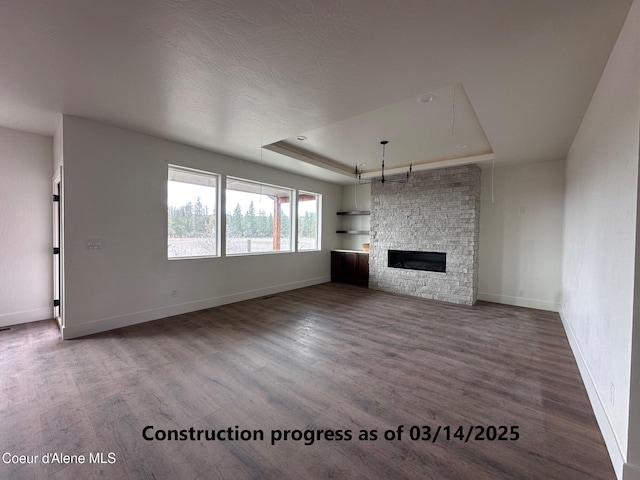 unfurnished living room featuring a stone fireplace, a raised ceiling, wood finished floors, and baseboards