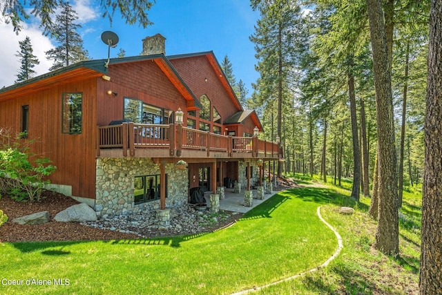 back of property with a patio, a chimney, stone siding, a deck, and a lawn