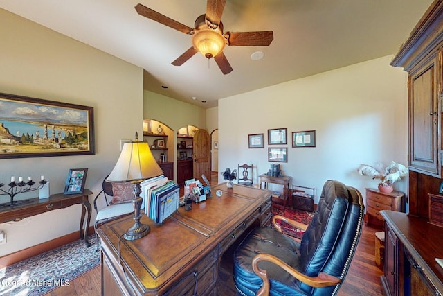 office space with arched walkways, a ceiling fan, and wood finished floors