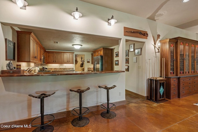 kitchen with stainless steel fridge with ice dispenser, concrete floors, a kitchen breakfast bar, a peninsula, and dark countertops