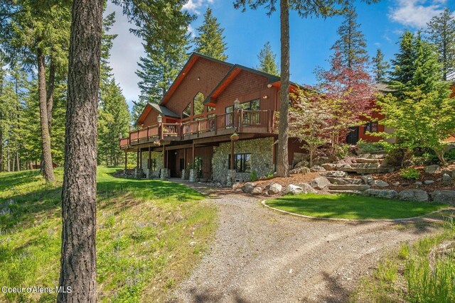 rear view of house featuring a yard, a wooden deck, stone siding, and dirt driveway