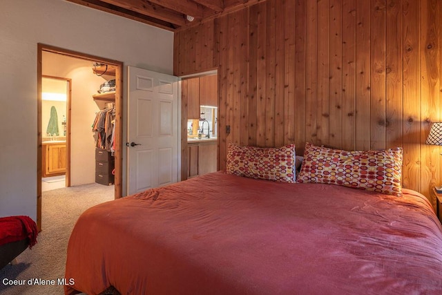 carpeted bedroom featuring wood walls, a walk in closet, sink, beam ceiling, and a closet