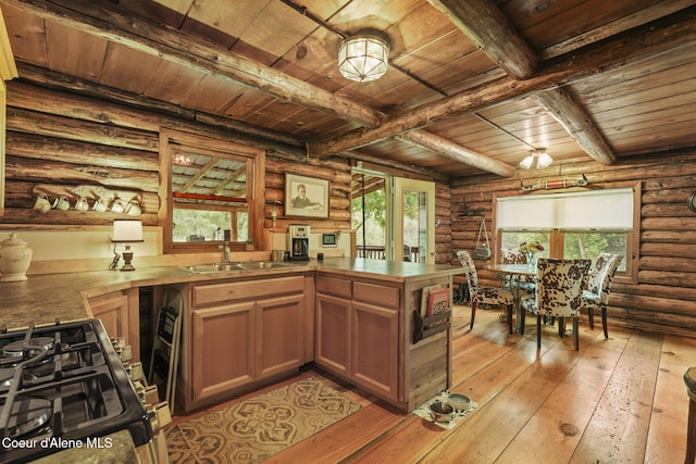 kitchen featuring light hardwood / wood-style flooring, stainless steel range with gas stovetop, sink, beamed ceiling, and rustic walls