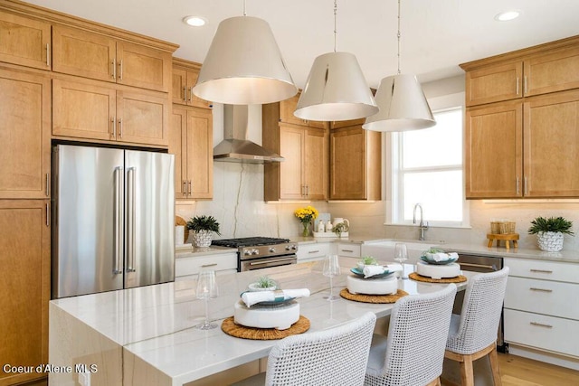 kitchen with wall chimney exhaust hood, appliances with stainless steel finishes, a kitchen island, pendant lighting, and light stone countertops