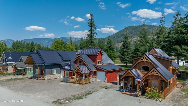 rustic home with stone siding, metal roof, a porch, a mountain view, and driveway