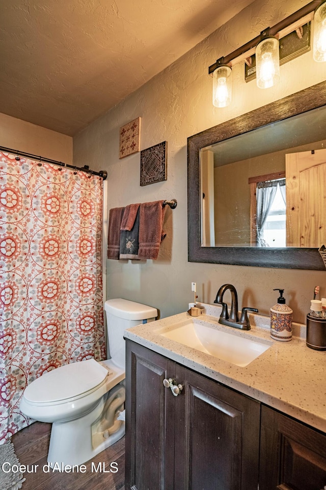 bathroom with vanity, a textured wall, toilet, and a shower with shower curtain