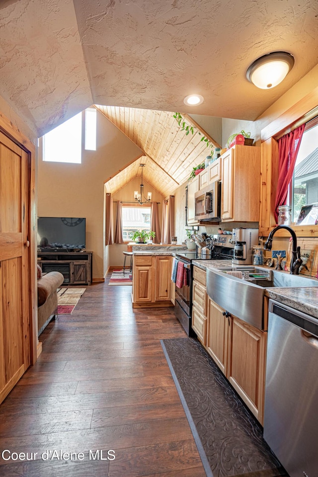 kitchen featuring appliances with stainless steel finishes, vaulted ceiling, a sink, a peninsula, and dark wood-type flooring