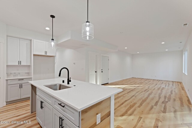 kitchen with sink, light wood-type flooring, a kitchen island with sink, and decorative light fixtures