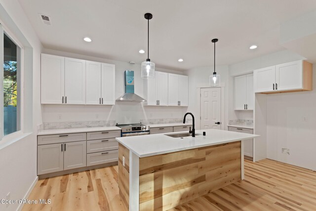 kitchen with light hardwood / wood-style flooring, sink, stainless steel electric range oven, a kitchen island with sink, and wall chimney exhaust hood