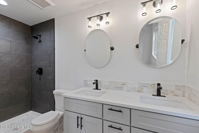 bathroom featuring dual vanity, toilet, and tiled shower