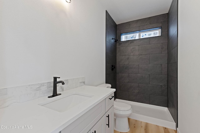 bathroom with tiled shower, wood-type flooring, toilet, and vanity