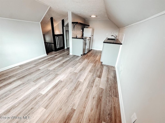 unfurnished living room with sink, light hardwood / wood-style floors, vaulted ceiling, and a textured ceiling