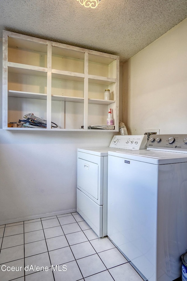 clothes washing area with washing machine and dryer, a textured ceiling, and light tile patterned floors