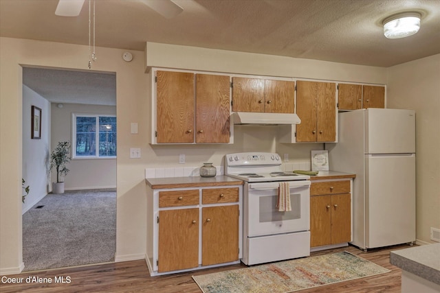 kitchen with white appliances, a textured ceiling, and light wood-type flooring