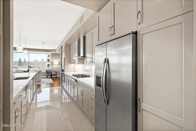 kitchen with sink, hanging light fixtures, stainless steel appliances, white cabinets, and wall chimney exhaust hood