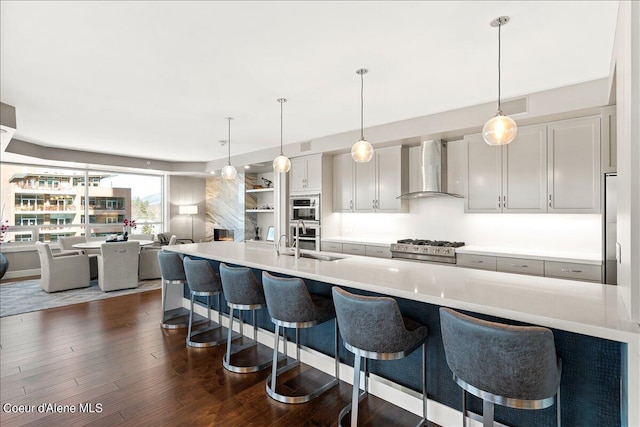 kitchen featuring wall chimney range hood, a kitchen bar, sink, and appliances with stainless steel finishes