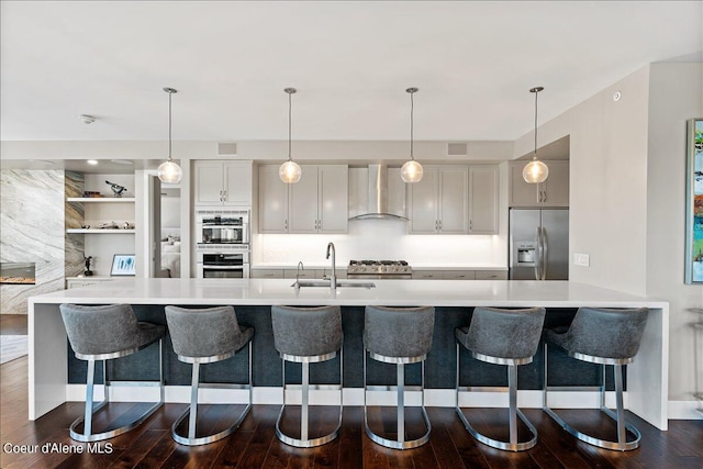 kitchen featuring wall chimney exhaust hood, stainless steel appliances, a breakfast bar area, and hanging light fixtures