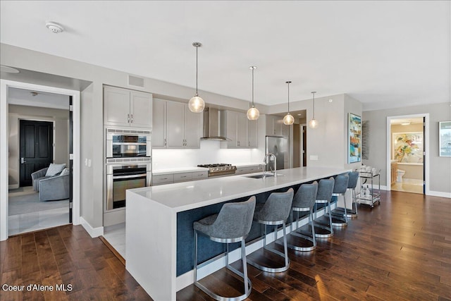 kitchen with a spacious island, wall chimney exhaust hood, a kitchen bar, hanging light fixtures, and appliances with stainless steel finishes