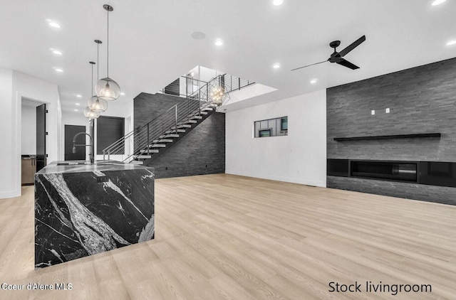 living room featuring ceiling fan, light hardwood / wood-style flooring, sink, and a large fireplace