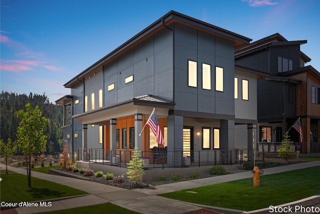 modern home with a porch, a standing seam roof, a yard, and metal roof