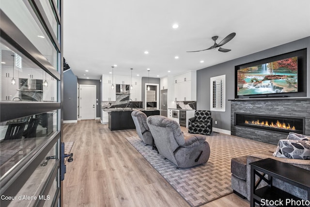 living room with recessed lighting, baseboards, a fireplace, and light wood finished floors