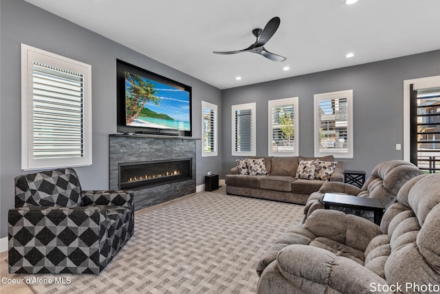 carpeted living area featuring baseboards, a stone fireplace, a ceiling fan, and recessed lighting