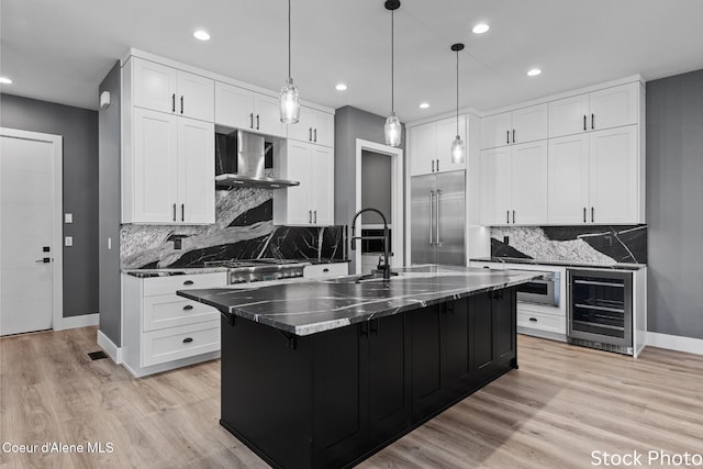 kitchen with beverage cooler, wall chimney range hood, built in fridge, and light wood-style flooring