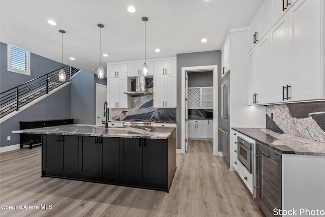 kitchen with light wood-style flooring, appliances with stainless steel finishes, white cabinetry, a sink, and wall chimney exhaust hood