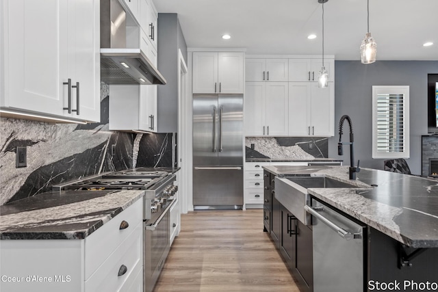 kitchen with wall chimney range hood, white cabinetry, high end appliances, and a sink