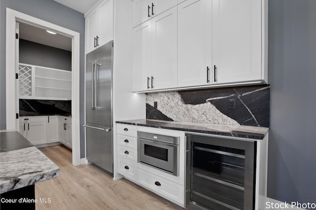 kitchen featuring wine cooler, white cabinets, high end fridge, light wood-type flooring, and decorative backsplash