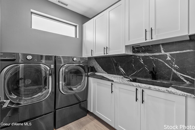 laundry room featuring a sink, visible vents, light wood-style floors, cabinet space, and washing machine and clothes dryer