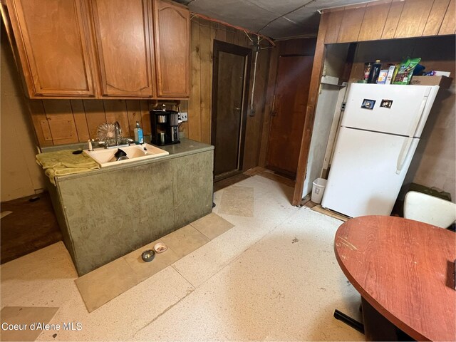 kitchen featuring wood walls, freestanding refrigerator, and brown cabinets