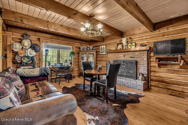 living room featuring a fireplace, wood-type flooring, beamed ceiling, an inviting chandelier, and log walls