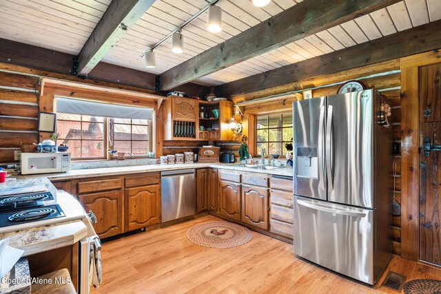 kitchen with beamed ceiling, track lighting, stainless steel appliances, light hardwood / wood-style floors, and rustic walls