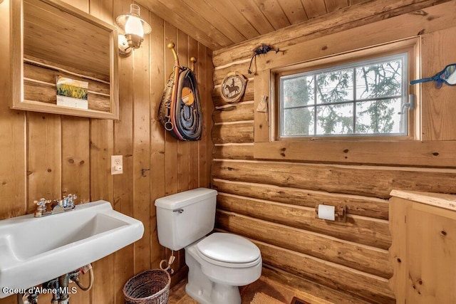 half bathroom featuring toilet, wood ceiling, a sink, and rustic walls