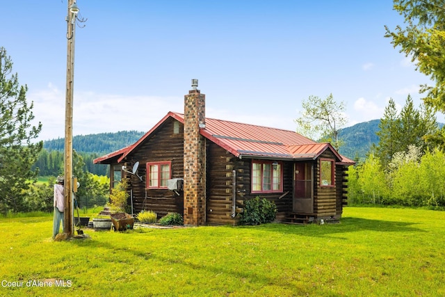 exterior space with metal roof, log exterior, a chimney, a standing seam roof, and a yard