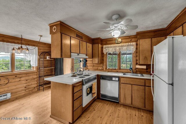 kitchen with decorative light fixtures, ceiling fan with notable chandelier, wooden walls, white appliances, and light hardwood / wood-style flooring