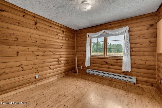 unfurnished room with log walls, a textured ceiling, a baseboard heating unit, and light hardwood / wood-style floors