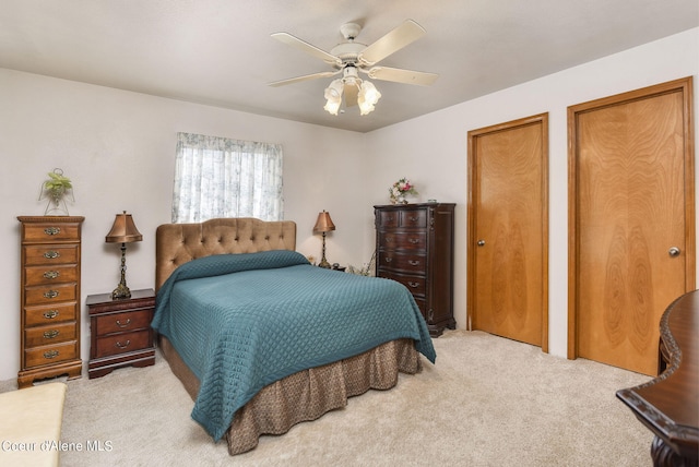 bedroom featuring multiple closets, light colored carpet, and a ceiling fan