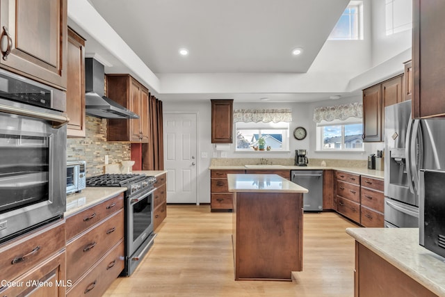 kitchen with light wood-style flooring, a center island, stainless steel appliances, wall chimney range hood, and a sink