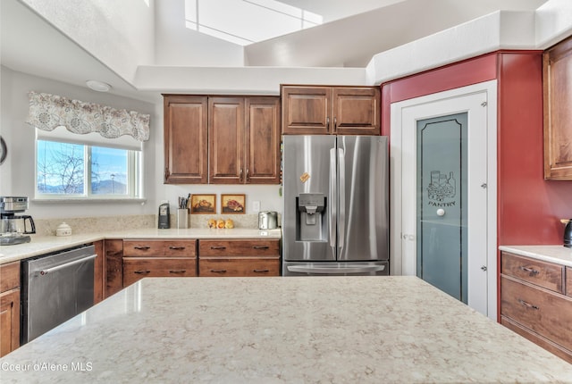 kitchen with stainless steel appliances, brown cabinets, and light stone counters