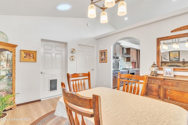 dining space featuring arched walkways, a chandelier, recessed lighting, light wood-style floors, and vaulted ceiling