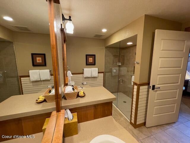 bathroom featuring a shower with shower door, vanity, tile patterned flooring, and a textured ceiling