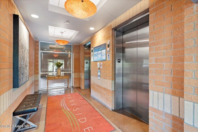 hallway with elevator, brick wall, and recessed lighting