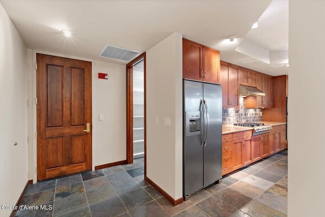 kitchen with under cabinet range hood, baseboards, light countertops, appliances with stainless steel finishes, and decorative backsplash