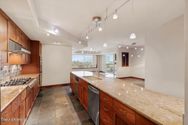 kitchen featuring tasteful backsplash, stone tile flooring, appliances with stainless steel finishes, a sink, and under cabinet range hood