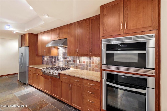 kitchen featuring under cabinet range hood, appliances with stainless steel finishes, brown cabinets, and backsplash